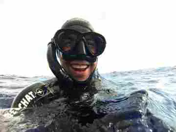 Freediver in the water wearing black freediving mask and black snorkel; smiling.